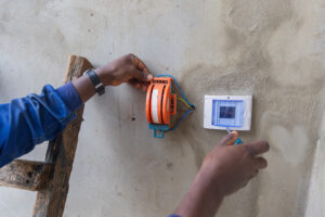 Foreground shot of an electrician's hands on a ladder opening a box on the wall